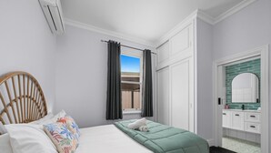 Een hotelkamer met een bed, een houten stoel, een raam met gordijnen, een badkamer met een spiegel en uitzicht.