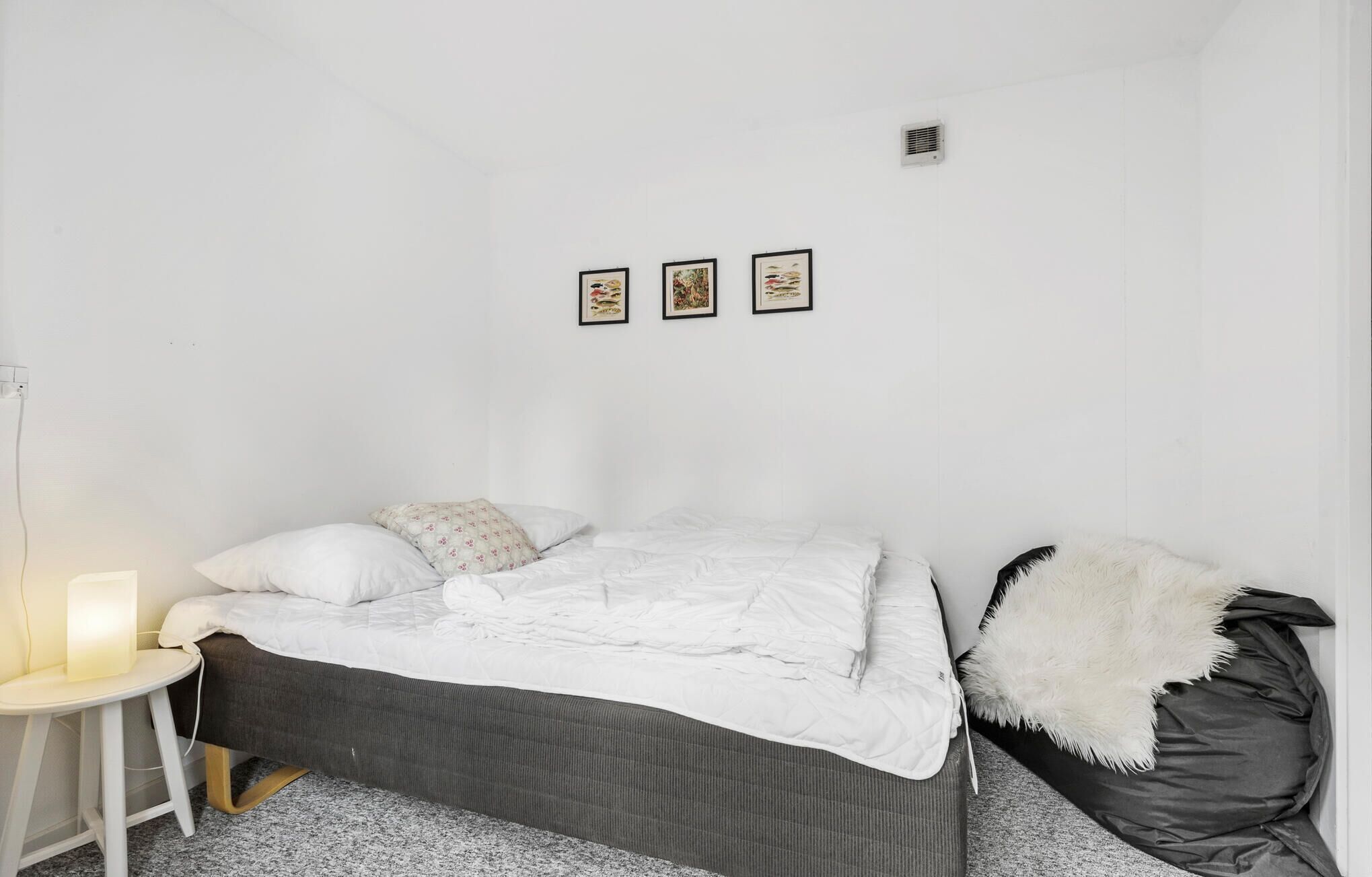 Une chambre à coucher avec un lit, une table de chevet avec une lampe et trois tableaux encadrés accrochés au mur.