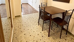 Uma sala de jantar com uma mesa e cadeiras, um quadro na parede e um corredor que leva a outro quarto.