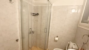Casa de banho com cabine de chuveiro em vidro, duas pias e sanita.