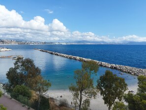 Blick auf die Küste mit einem steinernen Mole, klarem blauen Wasser und einer entfernten Skyline.