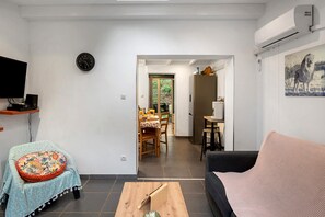 A living room with a TV, a clock, a dining area with a table and chairs, and a kitchen with a refrigerator.
