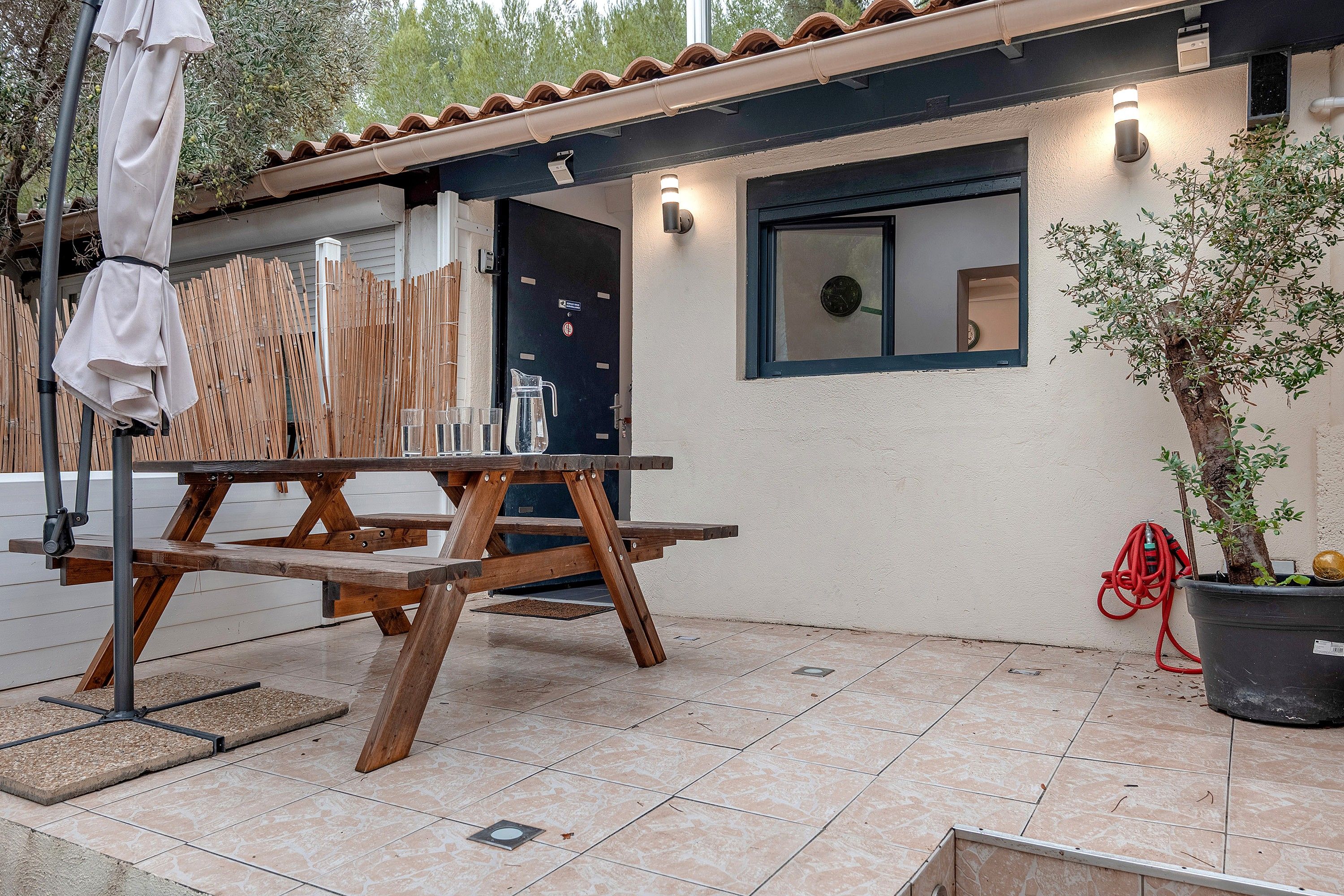 A patio with a wooden table and benches, a potted plant, and a door with a window.