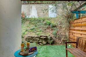 A patio area with a table set for two, a wooden bench, and a stone wall in the background.