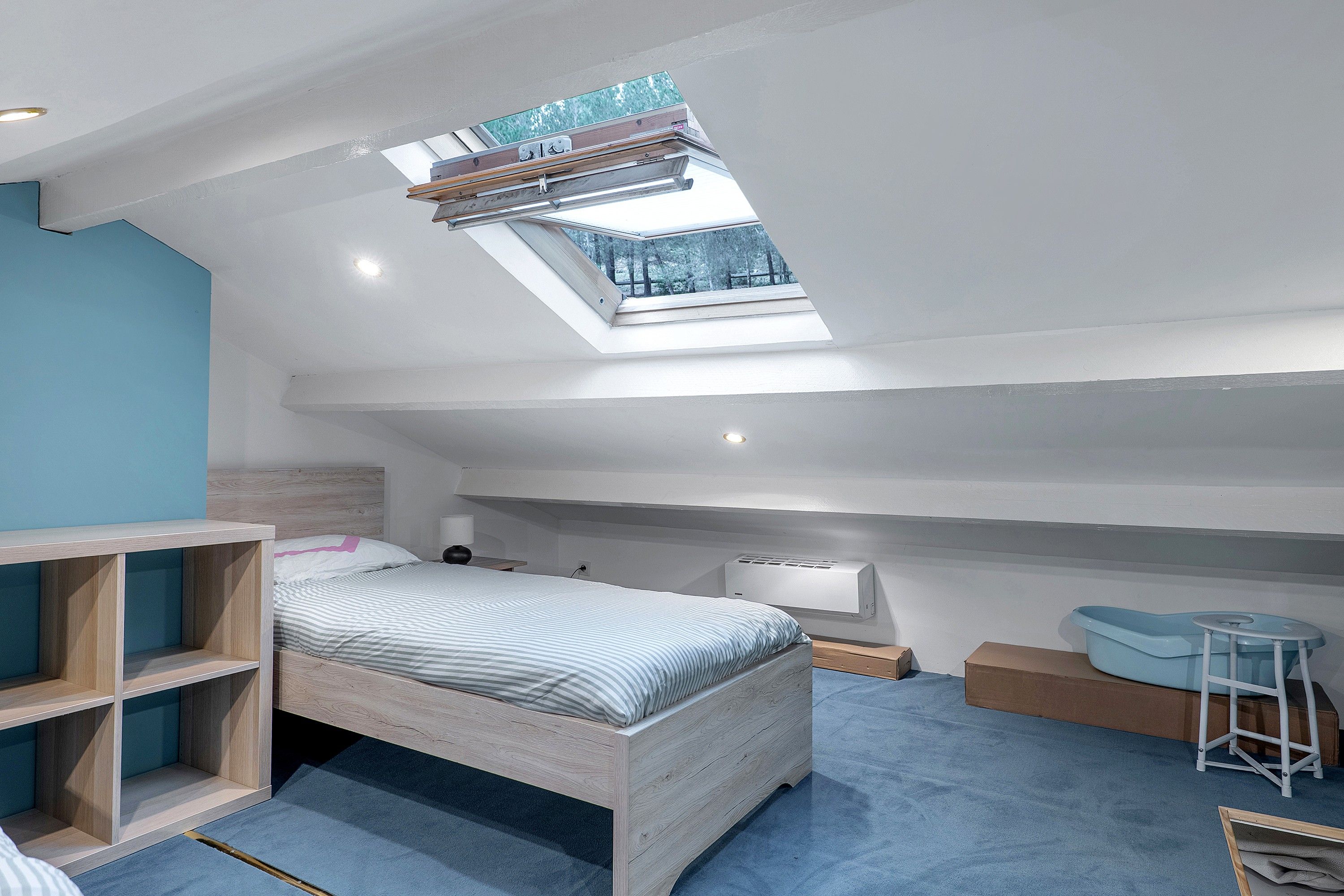 A bedroom with a skylight, a bed, a desk, and a chair.