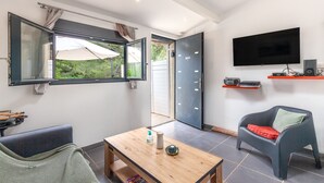 Ein Zimmer mit Fernseher, einem Tisch mit Flasche und Schale, einem Stuhl und einem Fenster mit Vorhängen.
