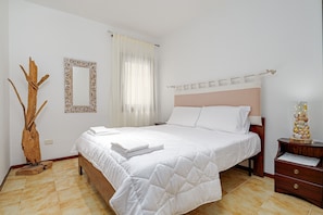 Ein Schlafzimmer mit einem Bett, einem Nachttisch, einem Spiegel und einer Zimmerpflanze.