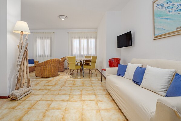 Una sala de estar con sofá, sillas, mesa y televisor.