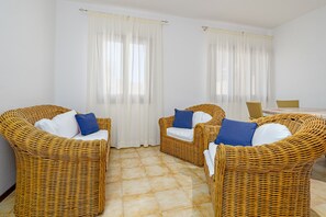 Una habitación con cuatro sillas de mimbre, dos cortinas blancas y un suelo de baldosas.