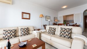 Ein Wohnzimmer mit Sofa, Couchtisch und einem Essbereich im Hintergrund.