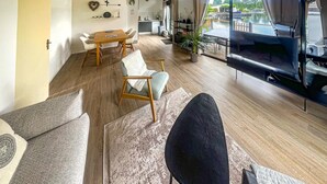 A modern living room with a wooden floor, a dining area with a wooden table and chairs, a black chair, and a view of a water body through large windows. - 2 bedroom beautiful home in Lemmer (Lemmer)