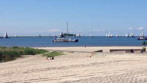 A beach with sailboats in the water, a sandy shore, and a few people.