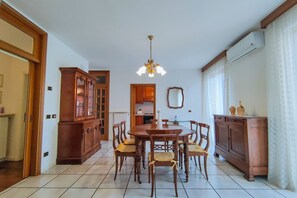 Zona pranzo con tavolo e sedie in legno, un lampadario e una cucina sullo sfondo.