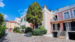 Eine gepflasterte Straße mit Gebäuden, einem Baum und einer Person auf einem Balkon.
