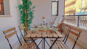 Een balkon met een houten tafel, stoelen, een bloempot en een fles.