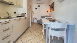 Een functionele keuken met een spoelbak, broodrooster en kastjes. Er is een eethoek met een tafel en stoelen.