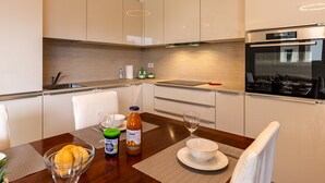 A modern kitchen with a dining area, featuring a built-in oven, stainless steel appliances, and a wooden dining table set with a bowl, glasses, and a bottle. - Apartment Luna by Interhome (Gravedona)