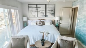 Una camera da letto con un letto grande, due comodini, un tavolino rotondo, due poltrone e vista sull'acqua, oltre a una porta.