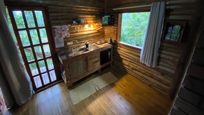 A rustic cabin with a wooden interior, a kitchen area with a sink and countertop, and a view of greenery outside. - Chalé Tucano Eco.hospedagem - Virado Para o Nascer do Sol, com uma Vista Linda (Praia Grande)