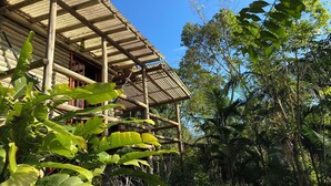 A wooden structure with a sloped roof, surrounded by lush greenery and trees. - Chalé Tucano Eco.hospedagem - Virado Para o Nascer do Sol, com uma Vista Linda (Praia Grande)