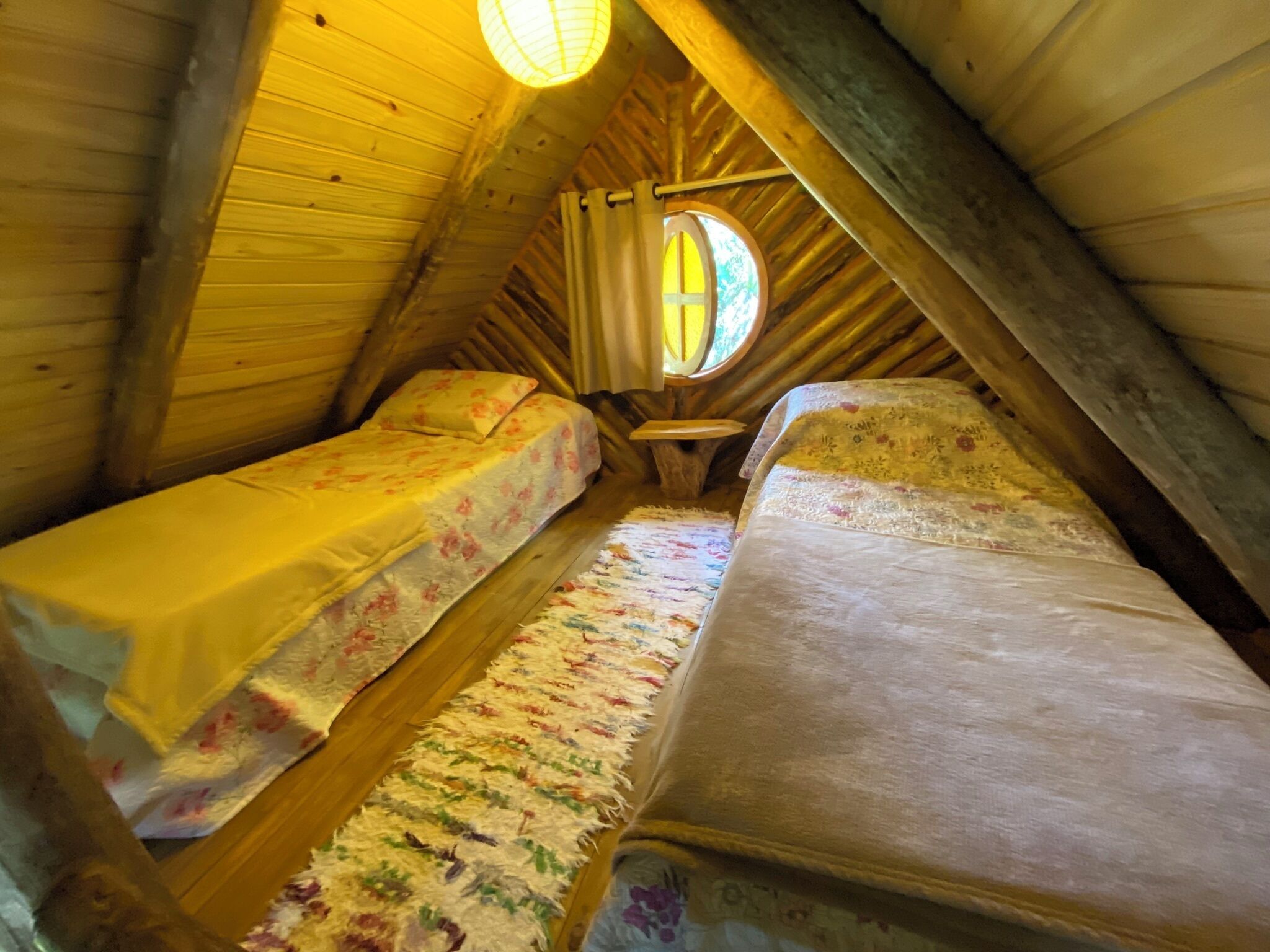 Een gezellige slaapkamer onder de dakpannen met twee bedden, een tafeltje en een raam dat voor natuurlijk licht zorgt.