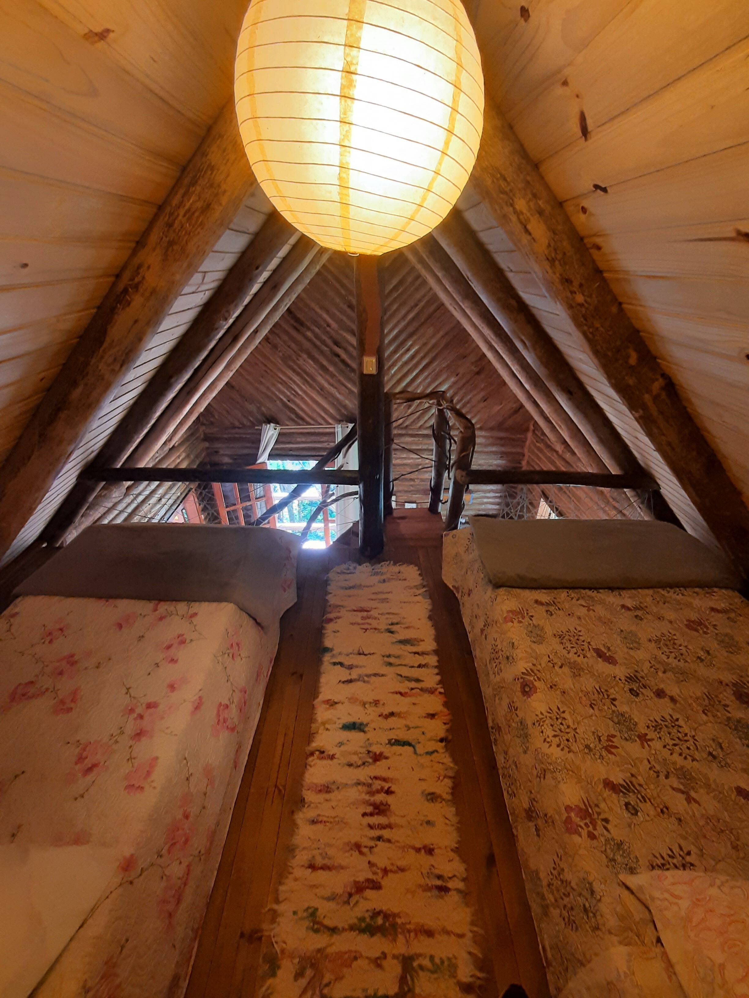 A cozy attic room with wooden beams, a large hanging lantern, and two beds with floral bedding.