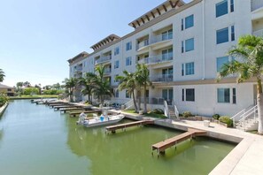 A marina with boats docked, a building with balconies, and palm trees. - Las Marinas #407 | Waterfront Condo • Boat Slip • 6 Minute Walk to Beach (South Padre Island)