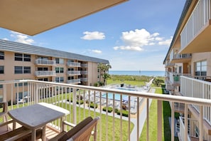 Un balcon avec une table et des chaises, donnant sur une piscine et offrant une vue sur l’océan.