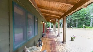 A covered porch with wooden beams, a wooden floor, and a view of a forested area.