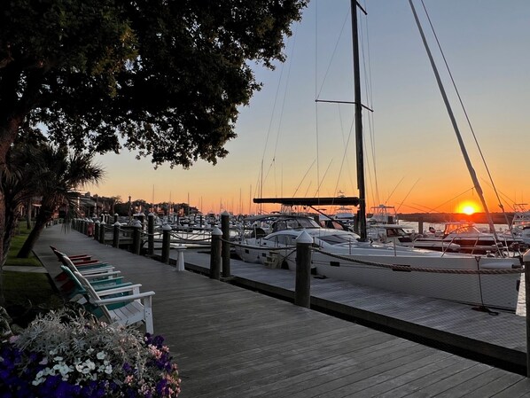 Un port de plaisance au coucher du soleil, avec des bateaux amarrés, une promenade en bois et une rangée de bancs.