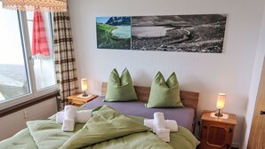 Une chambre d’hôtel avec un lit, deux tables de chevet, une fenêtre avec des rideaux et deux tableaux accrochés au mur.