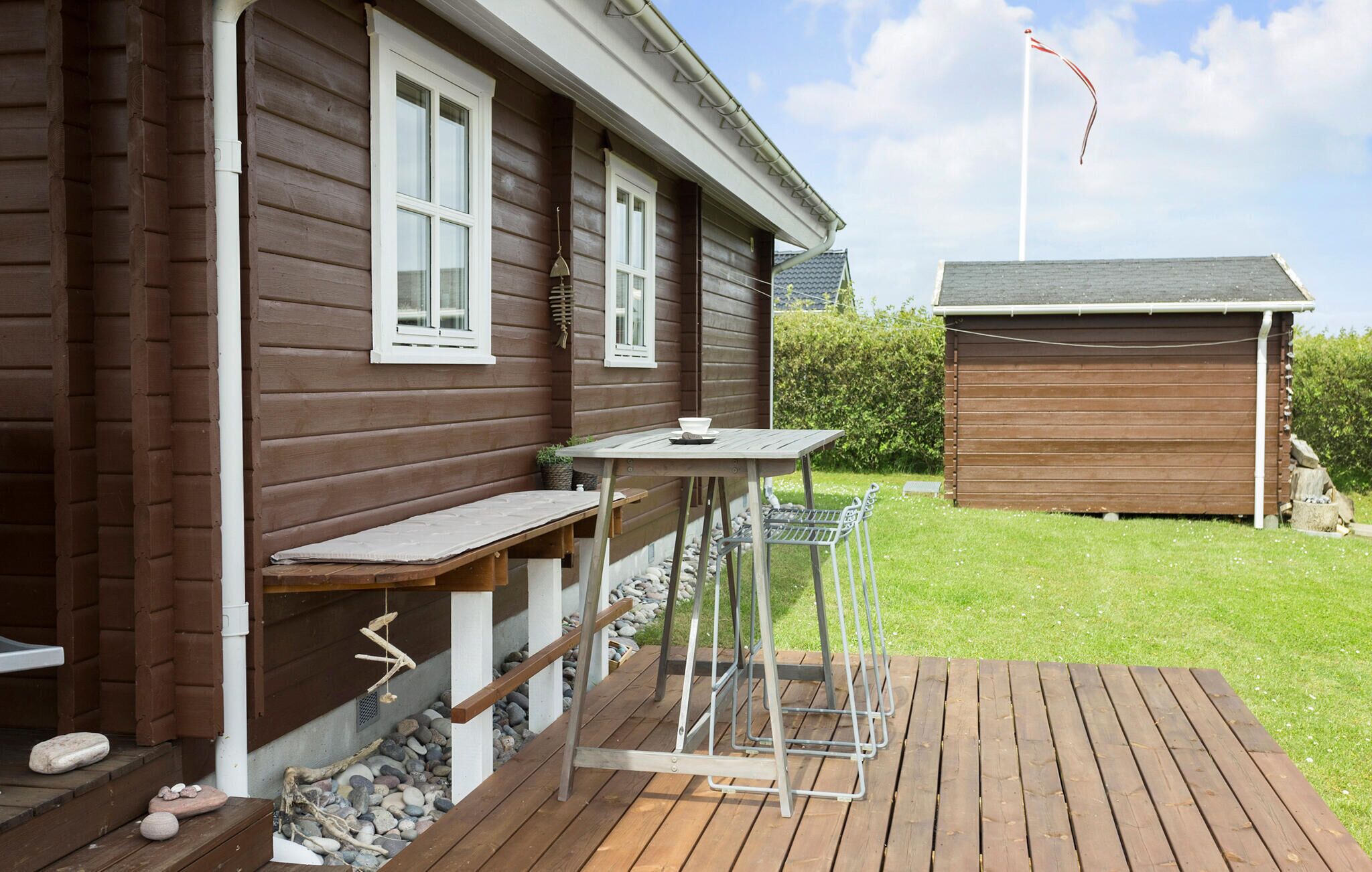 Une maison en bois avec une terrasse, une petite table et un banc.