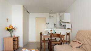 Un salon chaleureux avec un canapé, une table à manger dressée avec des tasses jaunes et un pichet, et une petite table en bois sur laquelle est posé un vase de fleurs.
