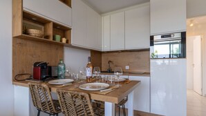 Una cocina moderna con armarios blancos, encimera de madera y horno empotrado. Hay sillas de mimbre y una mesa de comedor con platos y vasos.