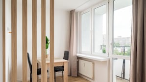 Una habitación moderna con suelo de madera, una mesa de comedor con sillas, una planta en maceta y ventanas amplias con cortinas.