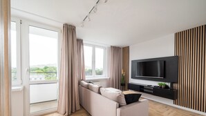 Una sala de estar moderna con un sofá, un televisor de pantalla plana y un ventanal con cortinas.