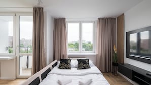 Una habitación de hotel moderna con una cama grande, dos almohadas, un televisor y un balcón con cortinas.
