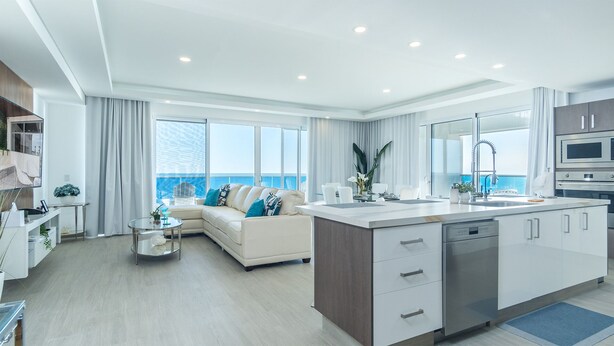 A modern kitchen with a central island, a dining area with a white sofa, and large windows offering a view of the ocean. - Impressive & beautiful 3 bedroom unit Ocean Front Encantame Velero-2301 (Puerto Peñasco)