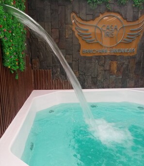 Un jacuzzi con agua fluyendo, rodeado por un muro de piedra y un letrero que dice "CASA IRIS BARICHA SANTANDER".