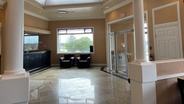 A lobby with a high ceiling, a reception desk, two chairs, a glass door entrance, and a large window with a view of trees. - ALMAC HOTEL Lac La Biche (Lac La Biche)