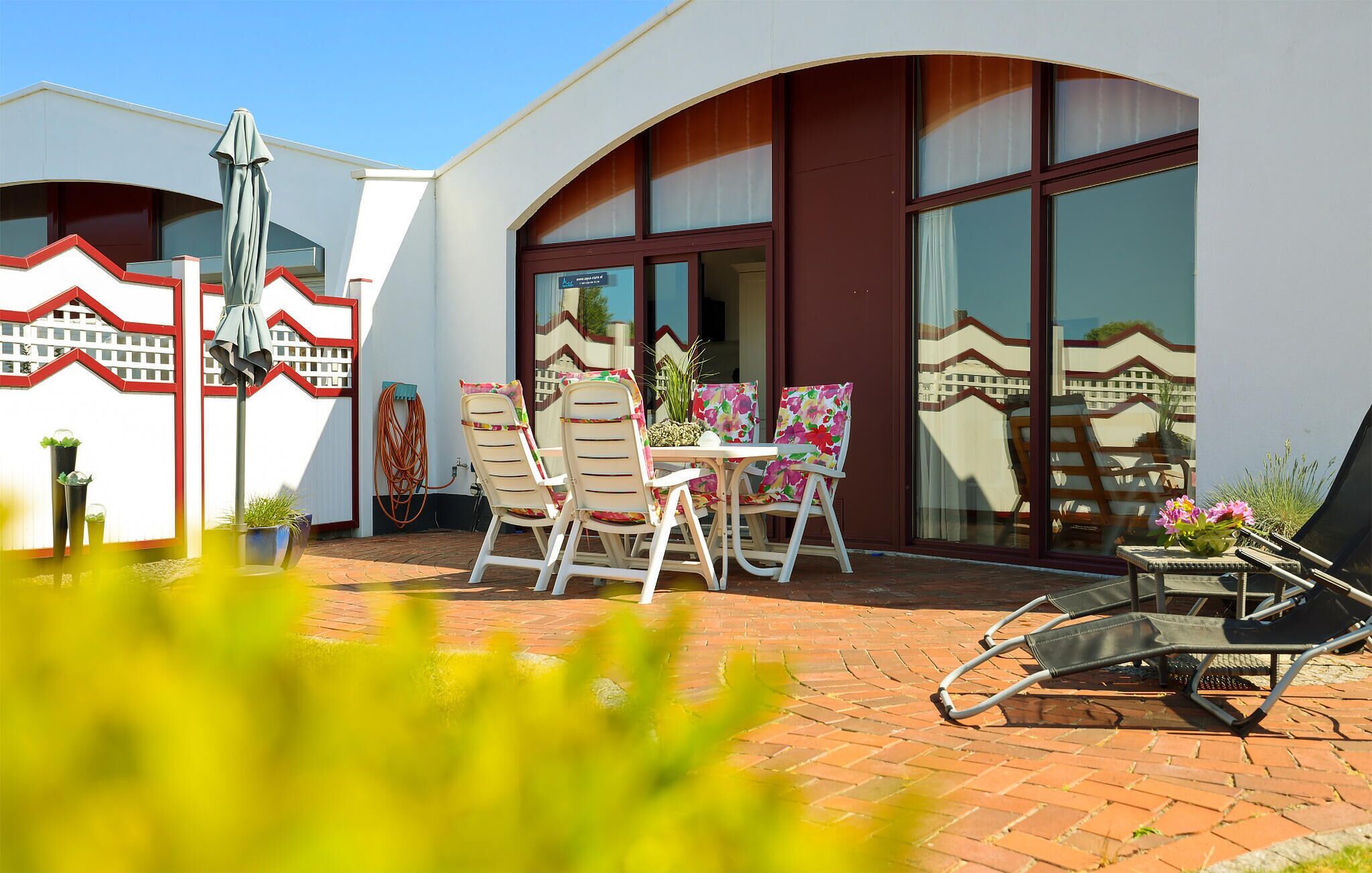 Eine Terrasse mit Tisch und Stühlen, einem Gartenschlauch und Kübelpflanzen.