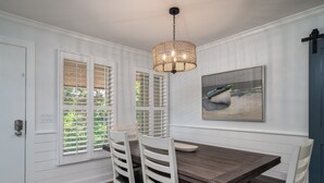A dining area with a wooden table, white chairs, a hanging light fixture, and a painting on the wall.