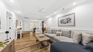 A spacious living room with a wooden floor, a grey sofa, a coffee table, and a ceiling fan.