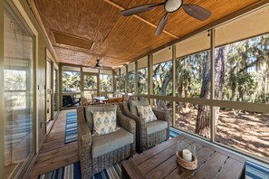 A covered outdoor seating area with wicker furniture and a table, overlooking a forested area. - 3 BR/2BA Cottage w/ Screen Porch! Dog Friendly! Amenity Access included (Seabrook Island)