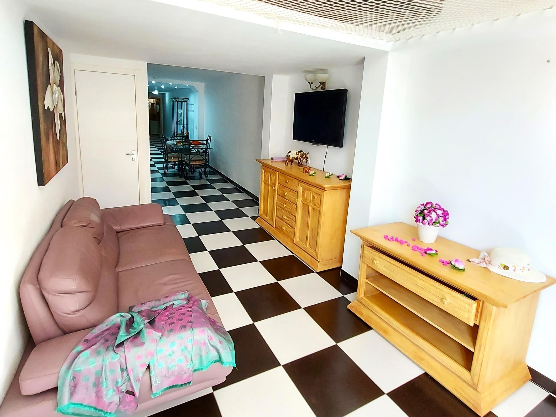 Ein Wohnzimmer mit Schachbrettfußboden, einer Couch, einem Holzschrank und einem an der Wand montierten Fernseher.