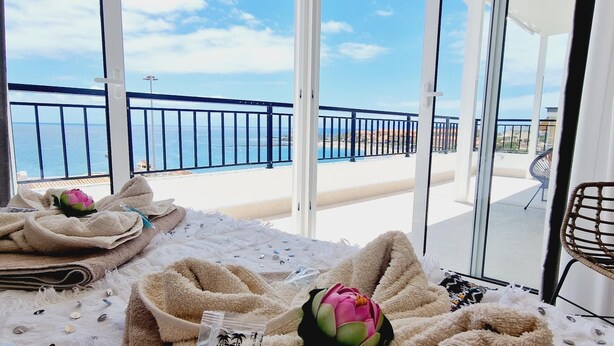 A balcony with a view of the sea, a chair, and towels with a shower gel package.