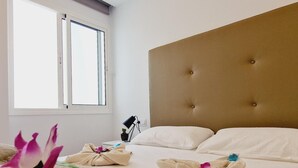 A hotel room with a large window, a tufted headboard, and a bed with white linens and towels.