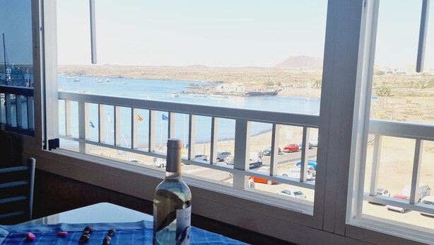 Een kamer met een groot raam met uitzicht op een strand en een jachthaven.