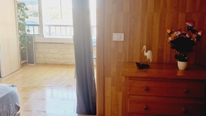 Een kamer met houten vloer, een houten dressoir, een tafeltje met een decoratieve vogel en bloemen, en uitzicht op het buitenlands landschap door een raam.