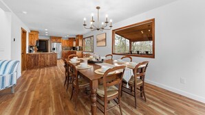 Uma cozinha espaçosa com armários de madeira, uma mesa de jantar posta com pratos e cadeiras, e um lustre.